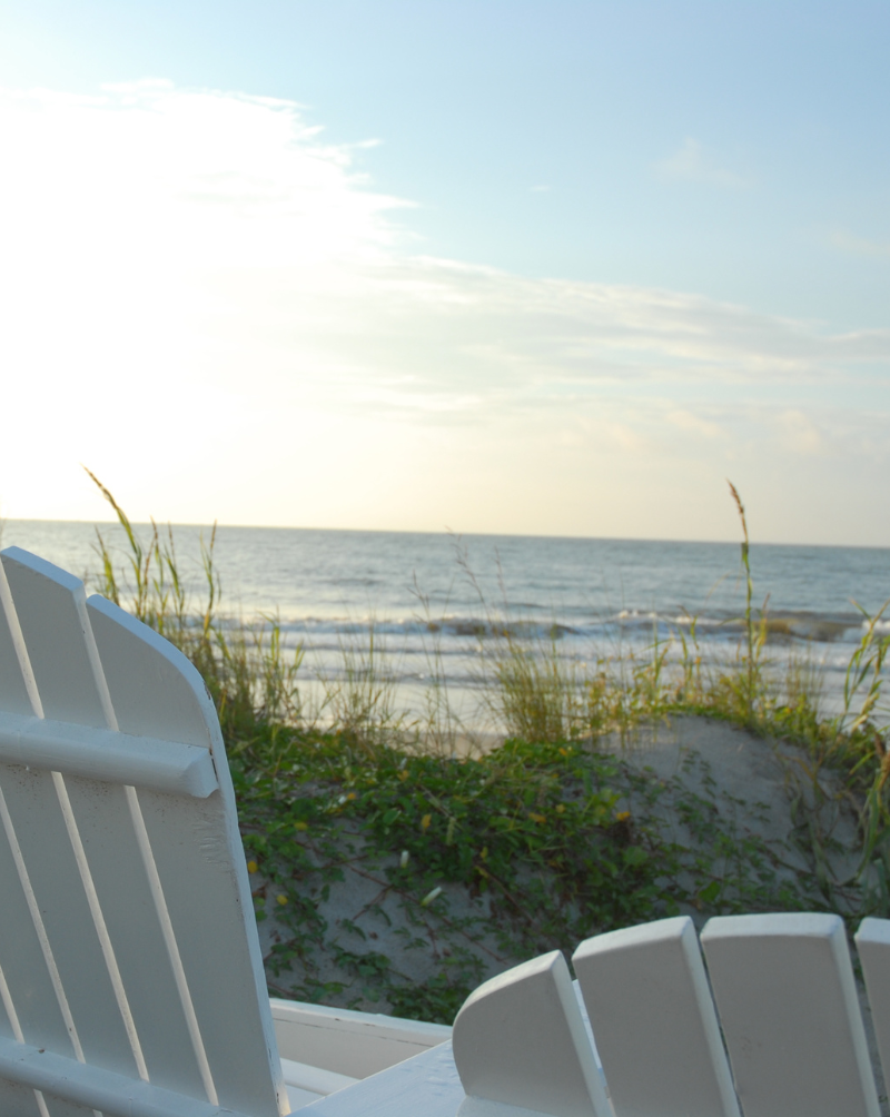 Chairs sitting behind a dune on the beach, looking over the ocean.
