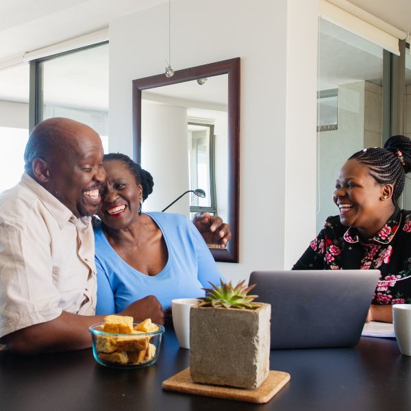 Middle-aged couple are hugging and laughing during a meeting with a younger woman with a laptop.